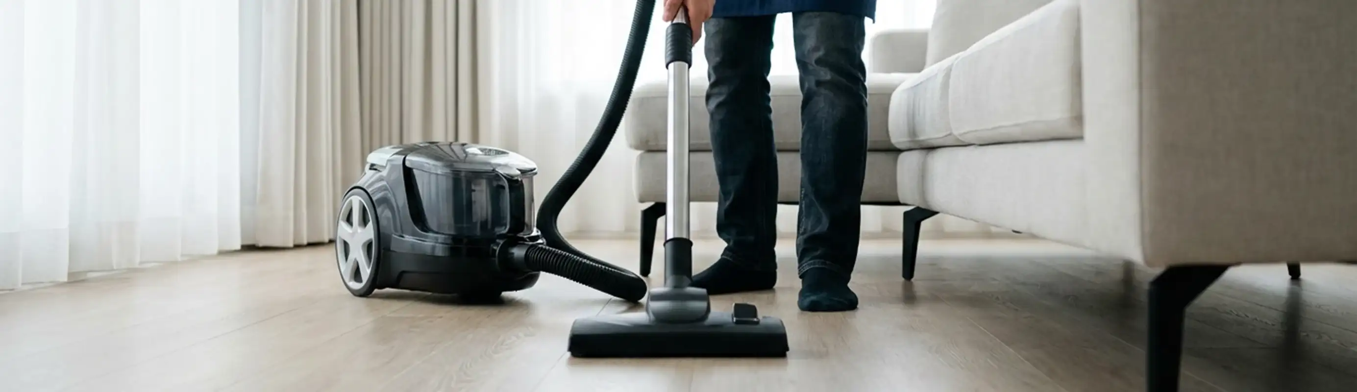 Professional house cleaner vacuuming a living room floor with a canister vacuum cleaner, Minneapolis, MN.