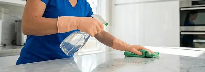 Maid service worker spraying and wiping a kitchen countertop with a microfiber cloth for sanitizing, Minneapolis, MN.