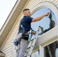 Professional window cleaner on a ladder using a squeegee to clean an exterior arched window, Minneapolis, MN.