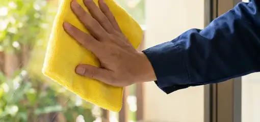 House cleaner wiping a glass window with a yellow microfiber cloth for streak-free cleaning, Minneapolis, MN.